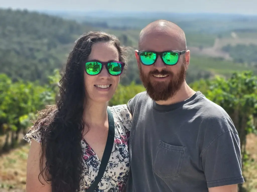 Couple with sunglasses smiling in front of vineyards in Italy.