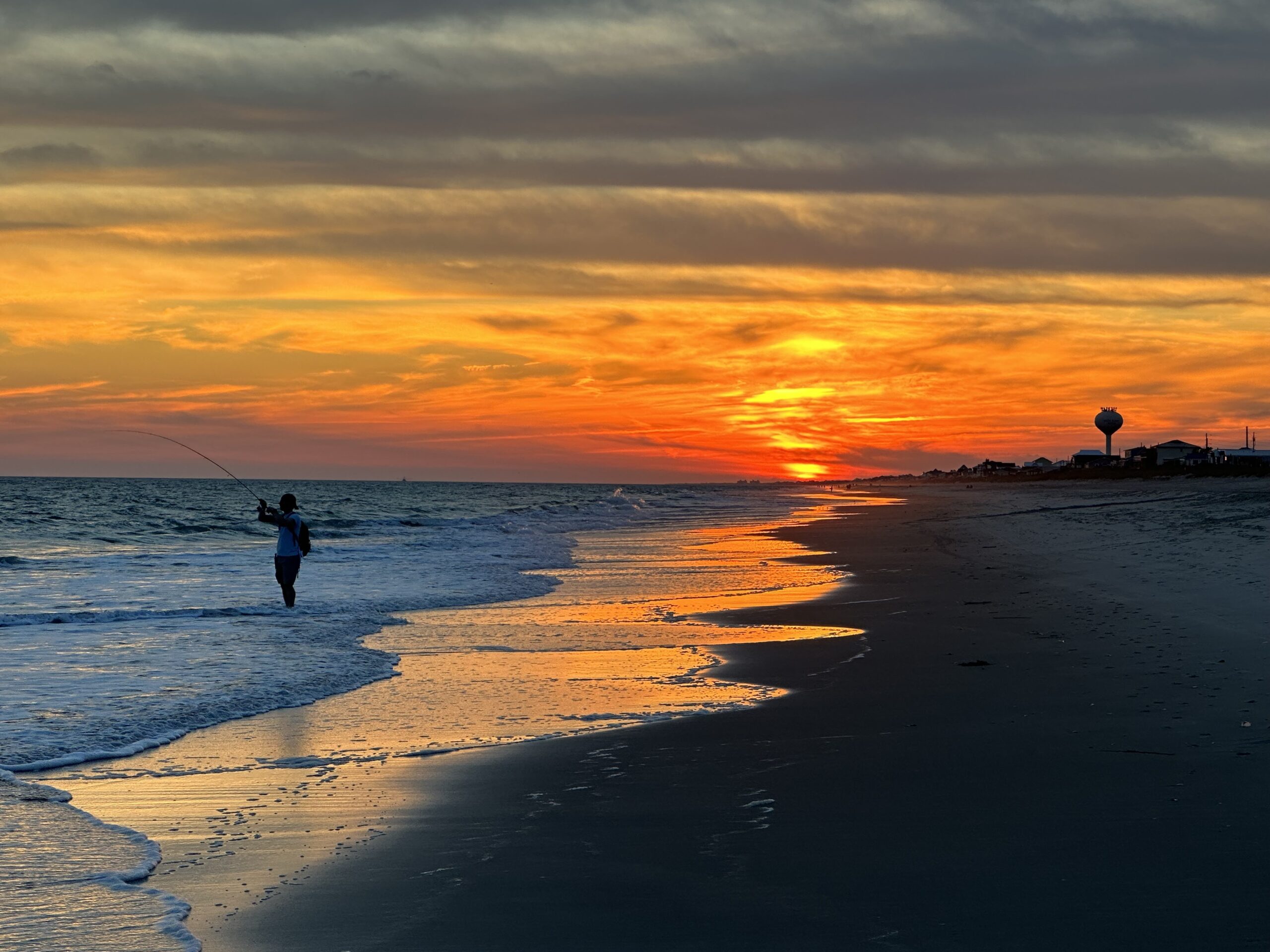 Ocean sand and waves during sunrise with a fisherman in the water.