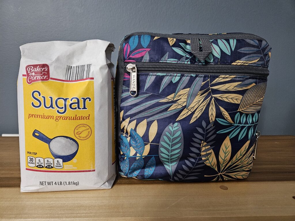 Photo of a folded up duffle bag next to a bag of sugar to show size parameters