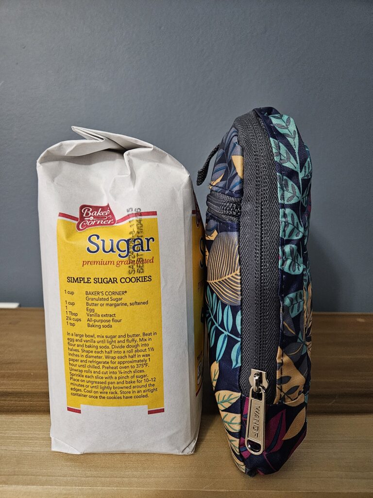 Photo of a folded up duffle bag from the side, up against the side of a bag of sugar.