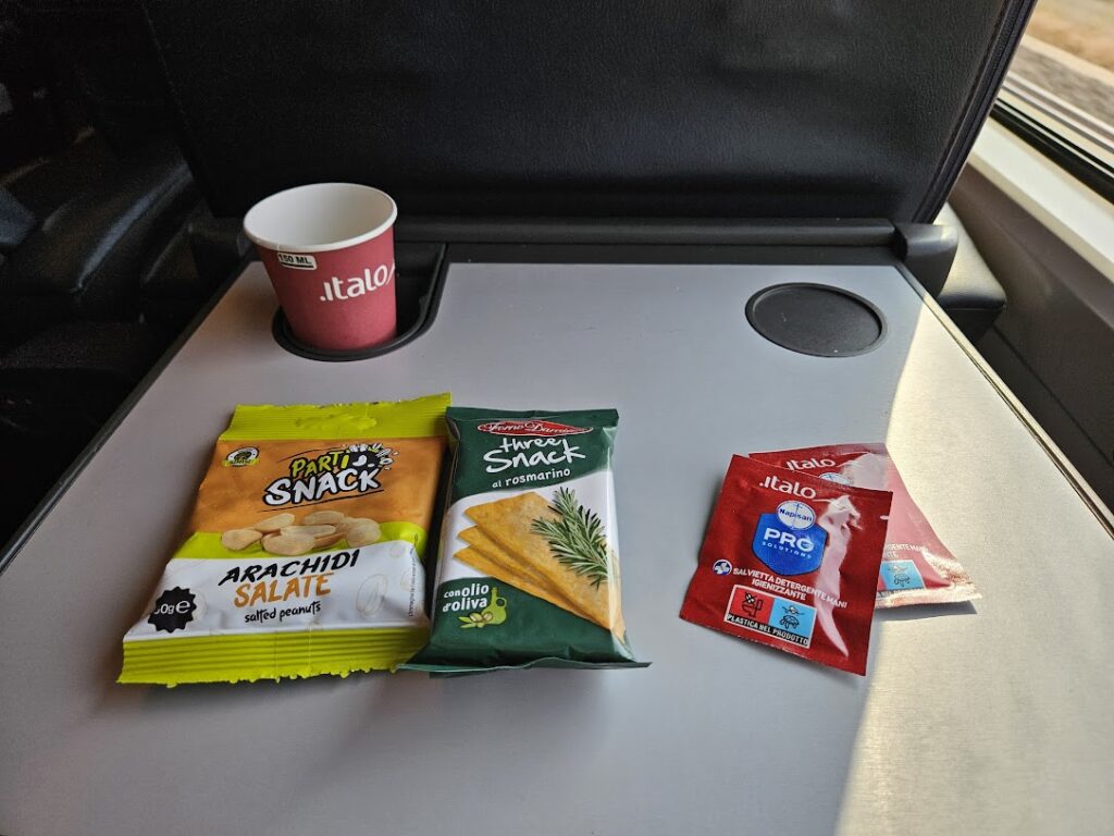 Picture of tray table on Italo train with a paper cup and various snacks