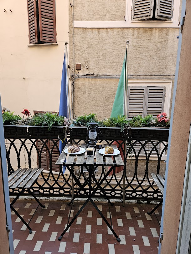 View of Parma, Italy AirBNB balcony showing a table and chairs with two croissants and espressos and flower boxes on the railing