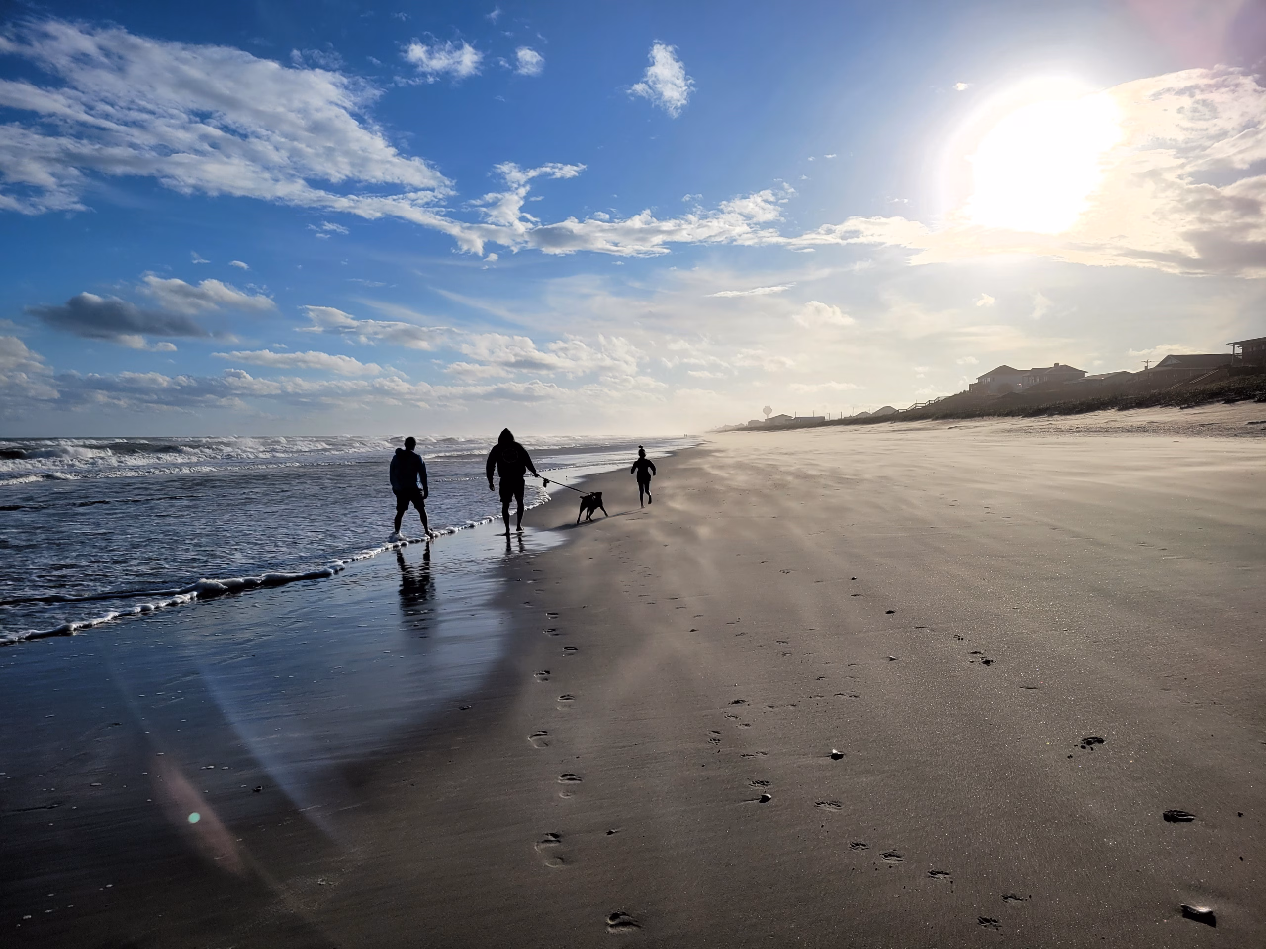 Family and dog walking down a beach on the Crystal Coast, sun high in the sky.