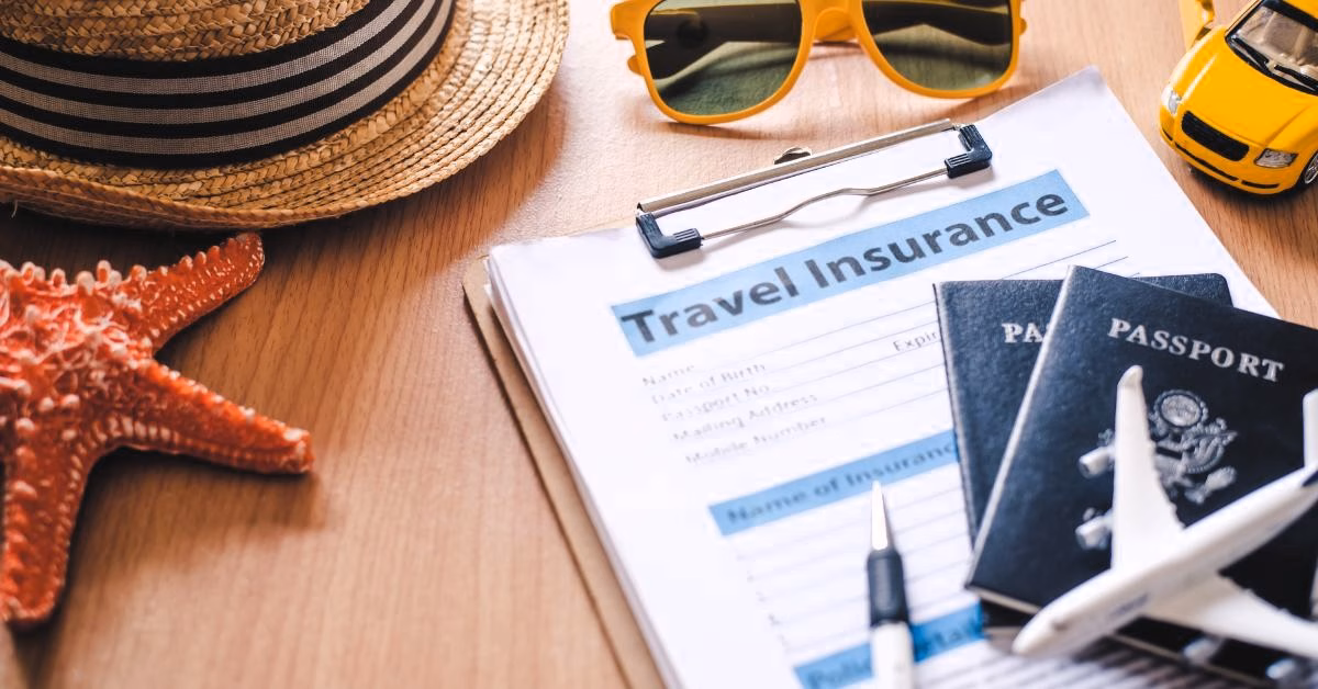 A desk with a clip board reading "Travel Insurance", two passports, a starfish, sunglasses, and beach hat.